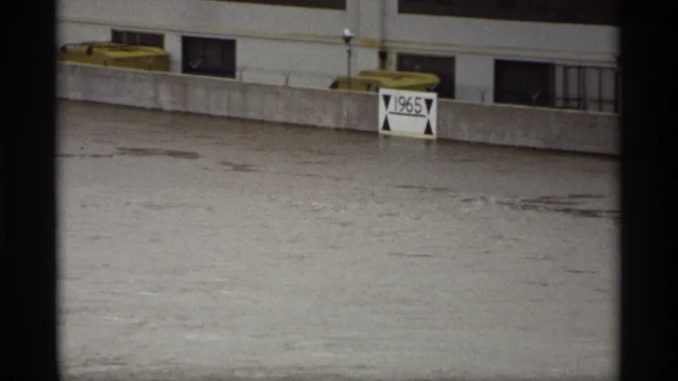 1969 Saint Paul floodwater surges past a concrete barrier, nearly submerging a white sign marked 1965.
