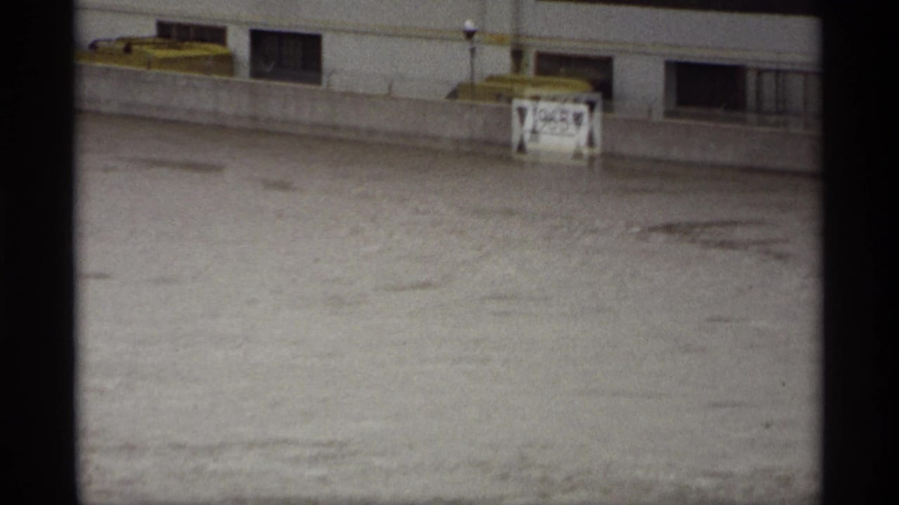 Murky floodwater moves below a concrete edge with a small marked sign behind it.