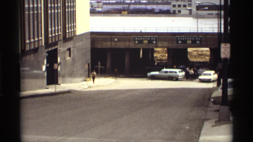 Saint Paul street scene from 1969 showing overhead road signs, classic vehicles by an underpass, and a small pedestrian figure.