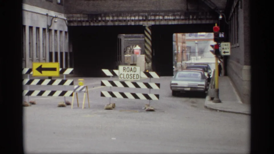 Saint Paul road closure in 1969 with barricades, ROAD CLOSED sign, grey sedan, one-way sign, and shaded underpass entrance.