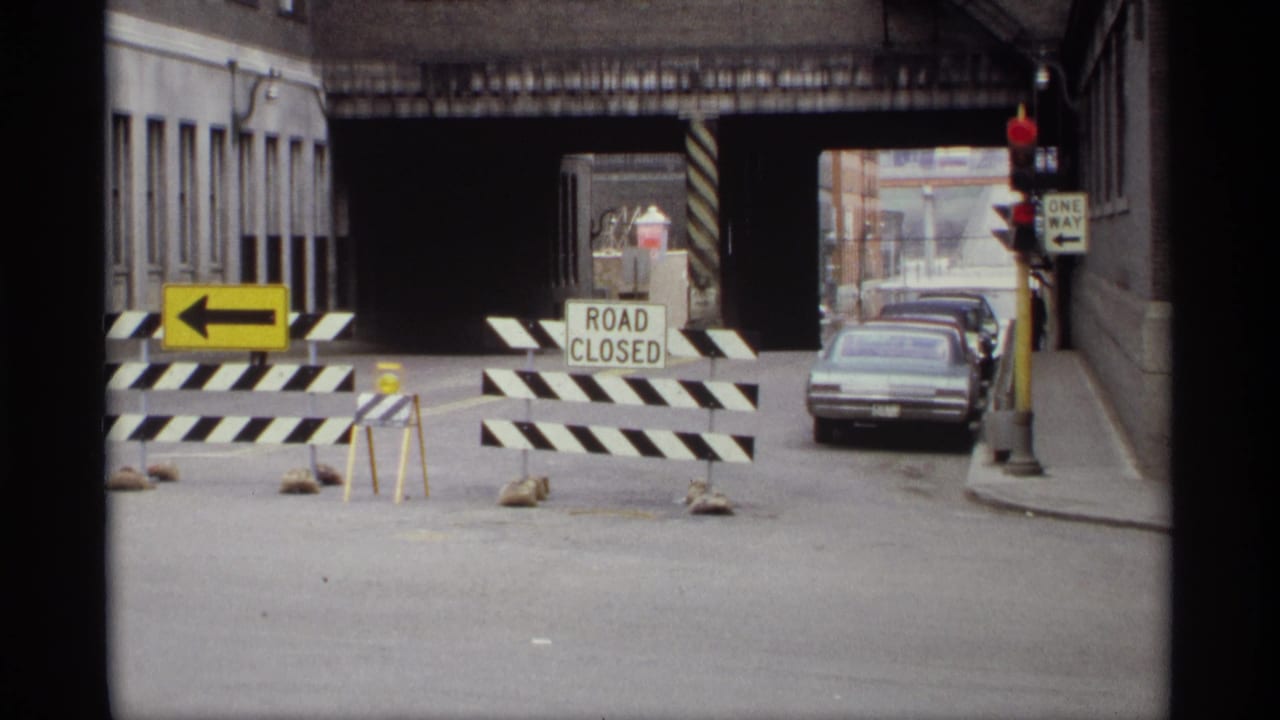 Saint Paul street view from 1969 showing striped Road Closed barricades, a one-way arrow, parked cars, and a bridge underpass.
