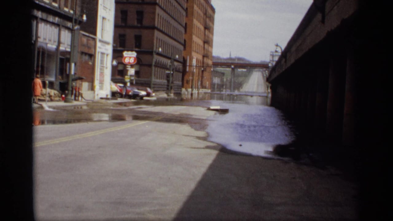 Wet city street with pooled water beside brick buildings and an overpass shadow.