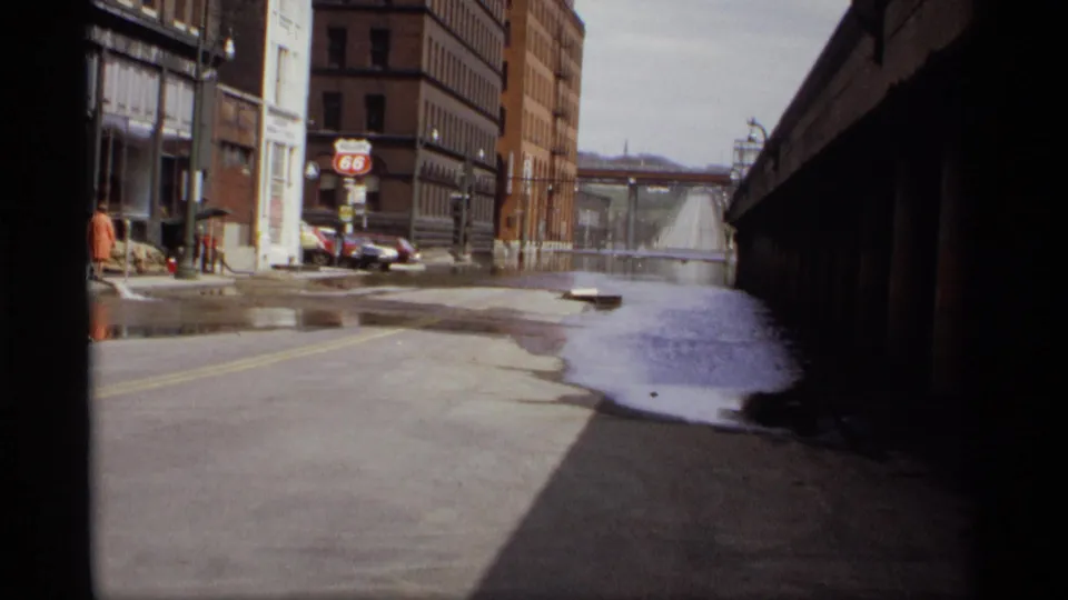1969 Saint Paul street scene with pooled water on the pavement, brick industrial buildings, parked cars, and a Route 66 sign in view.