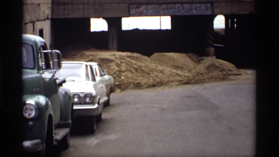 1969 Saint Paul frame with a green truck, white sedan, hay or straw piles, and a concrete overpass in a flooded-street context.