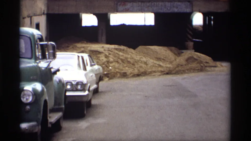 1969 Saint Paul frame showing a white car, green truck edge, overpass openings, and hay or straw piles along the street.