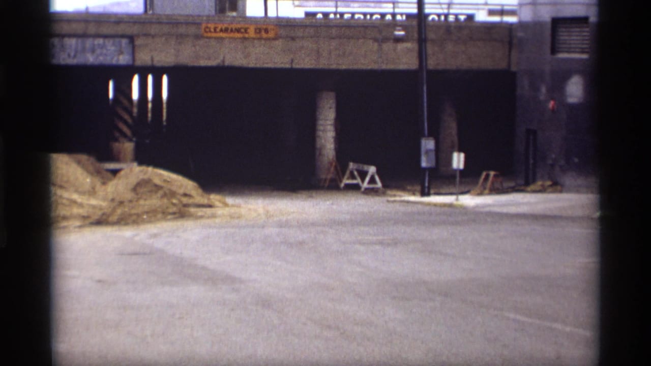 Underpass entrance with sand piles, clearance signs, street poles, and a pedestrian near the right edge.