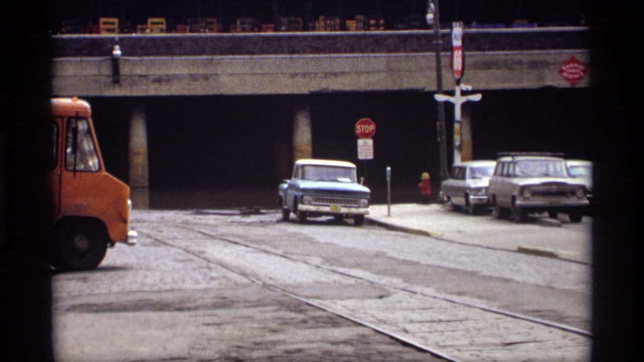 Street view beneath an overpass with a light blue pickup and other parked cars.