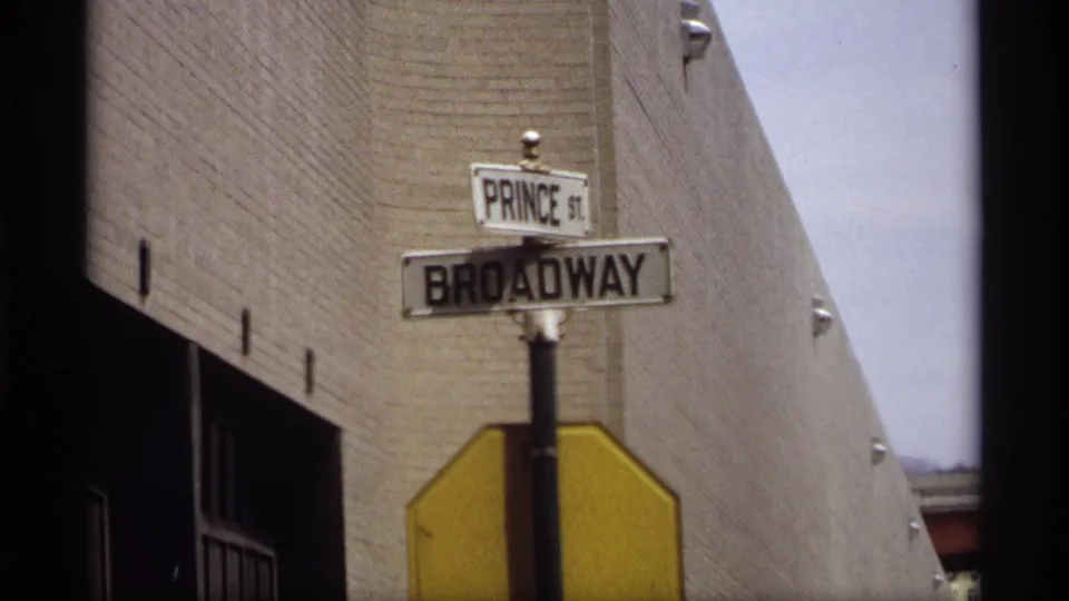 1969 Saint Paul close view of Prince St and Broadway street signs against a brick wall, with a yellow sign back below them.