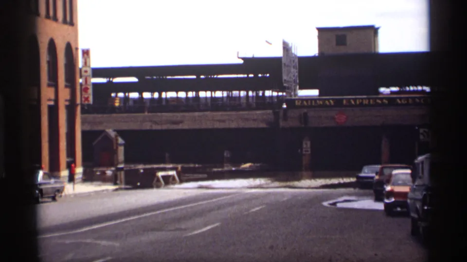 Saint Paul 1969 flood scene showing water across a street, classic cars, brick buildings, and a Railway Express Agency sign under elevated rail tracks.