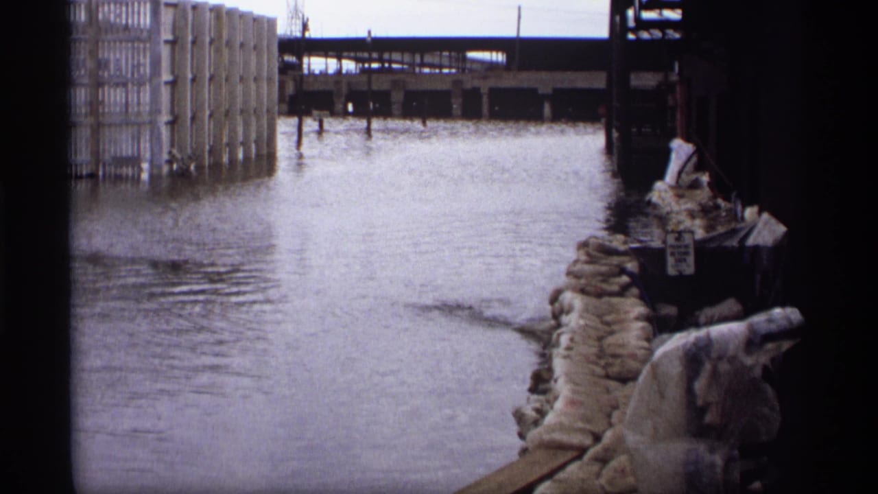 Floodwater beside industrial buildings with sandbags along the right edge.