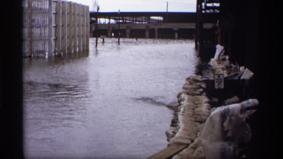 Saint Paul 1969 floodwater fills an industrial street or loading area, with sandbags lining the right side and rail structures in the background.