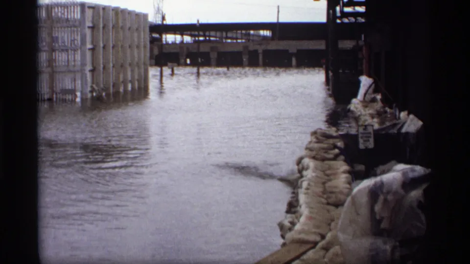 Saint Paul 1969 flood view showing water between industrial buildings, sandbags at right, and an elevated rail structure in the distance.