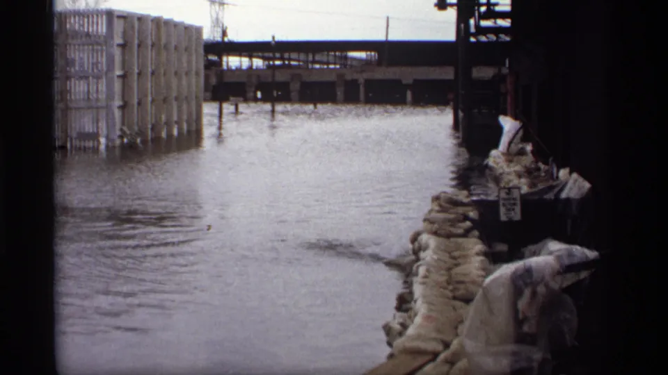 Saint Paul 1969 flood scene with sandbags at the right edge, high water across the frame, and industrial buildings beside an elevated rail line.