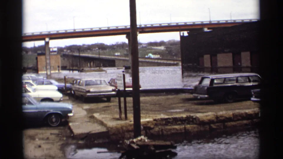 A wider 1969 Saint Paul view shows parked cars, a bridge, industrial buildings, and floodwater along a stone embankment.