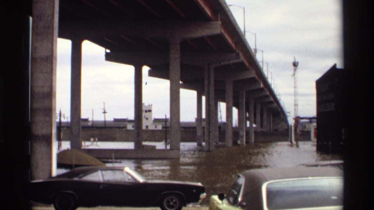 1969 Saint Paul flood scene showing muddy water under a concrete bridge, with period cars parked near the flooded riverfront.