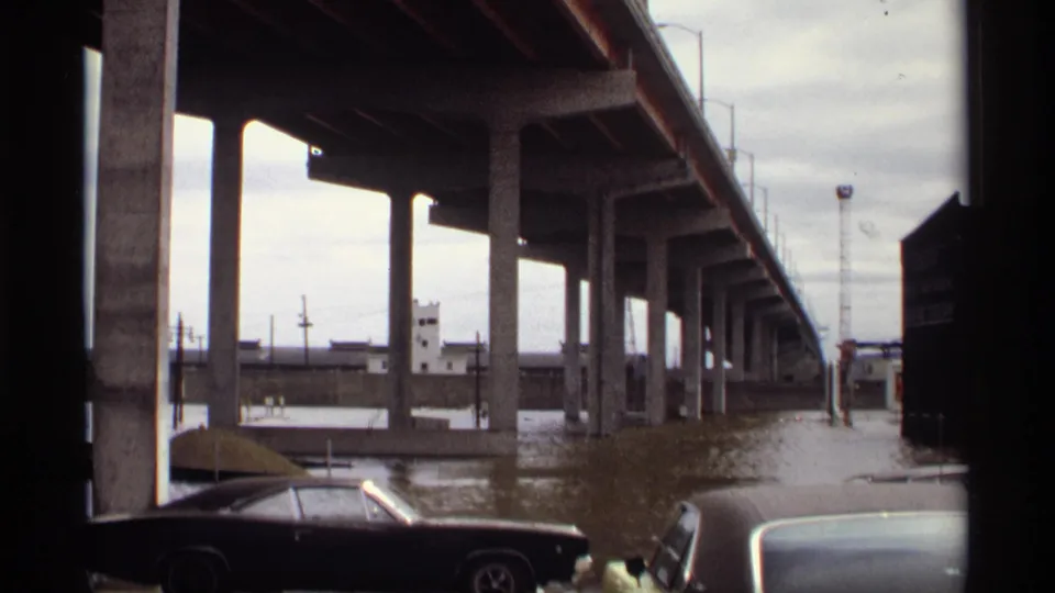 Saint Paul, Minnesota riverfront view from 1969 with floodwater under an elevated bridge and a dark period car in the foreground.