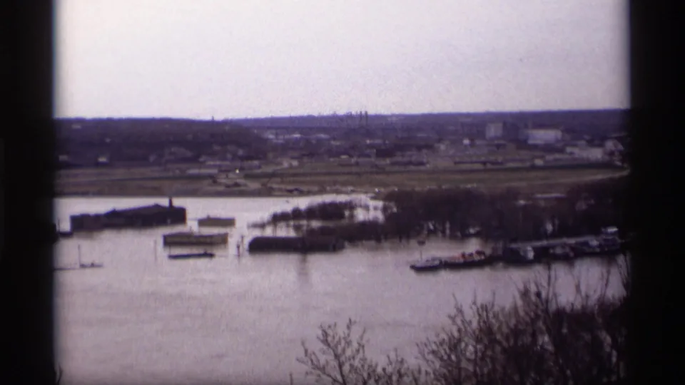 Wide Saint Paul Mississippi River view with barges, shoreline structures, and a low distant skyline.