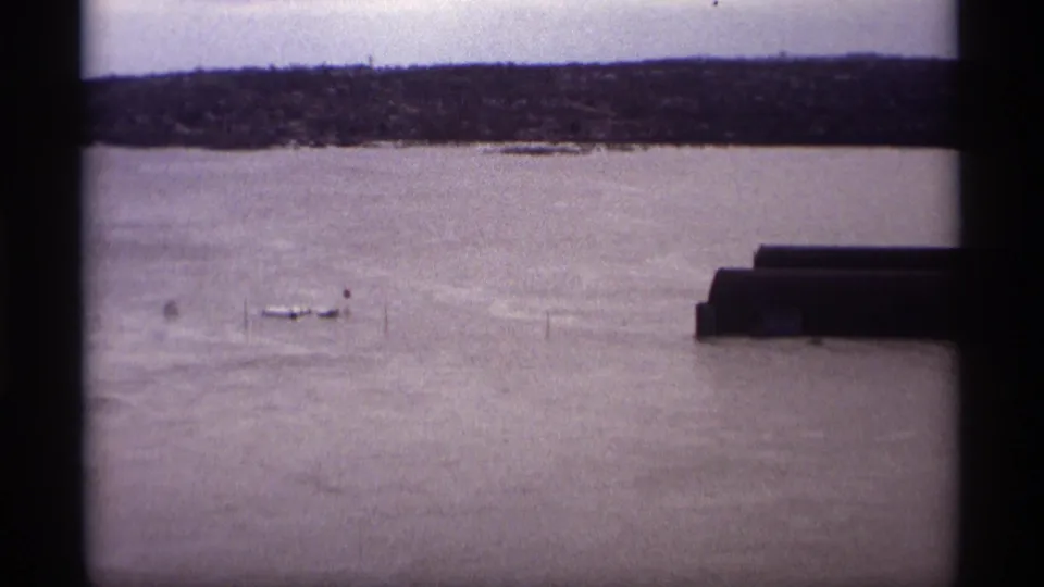 Saint Paul flood scene on 8mm film showing high water around small boats and posts beneath a cloudy sky in 1969.