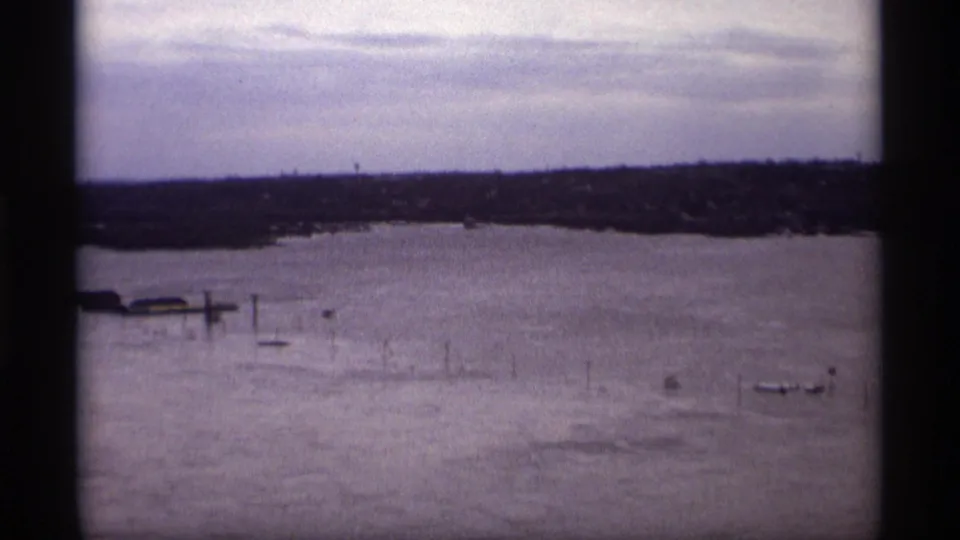Elevated 1969 home-movie view over a flooded Saint Paul river area with scattered posts, small boats, and distant land.
