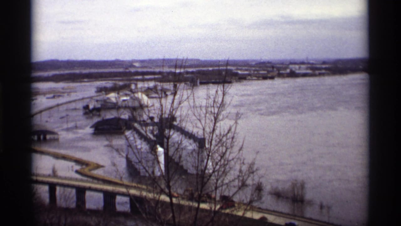 Wide elevated view of flooded river, bridge, bare trees, and submerged riverside roads.