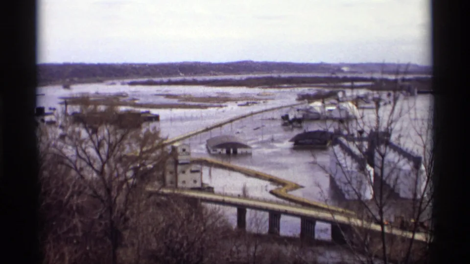 Elevated 1969 Saint Paul view of floodwater surrounding riverside buildings and a bridge, framed by leafless trees.