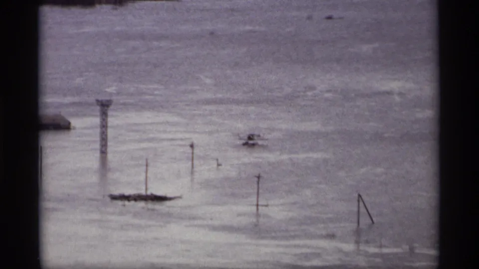 Wide 1969 Saint Paul flood view showing water covering low ground with poles, small structures, and distant shoreline.