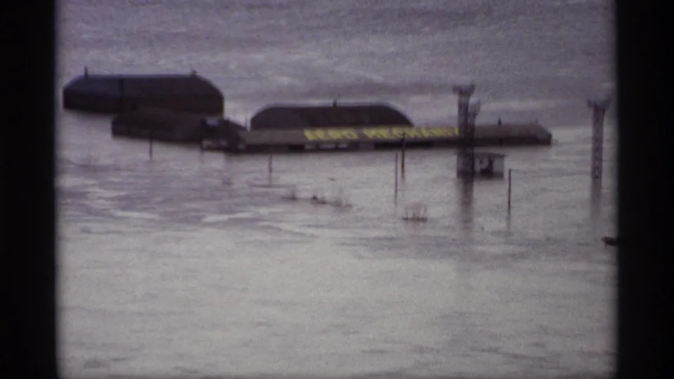 1969 Saint Paul flood frame showing submerged buildings, utility poles, and a readable Aero Mechanics sign near the waterline.