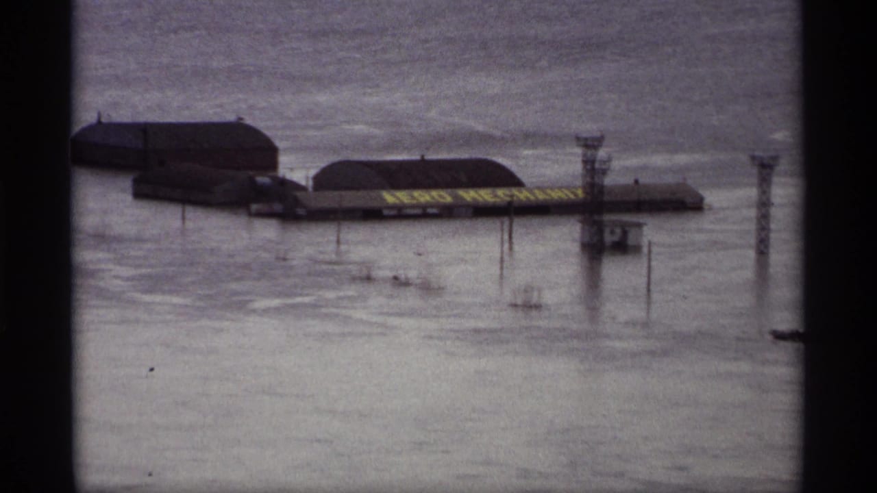 1969 Saint Paul floodwater surrounds riverside buildings, utility structures, and a partially visible AERO MECHANICS sign.