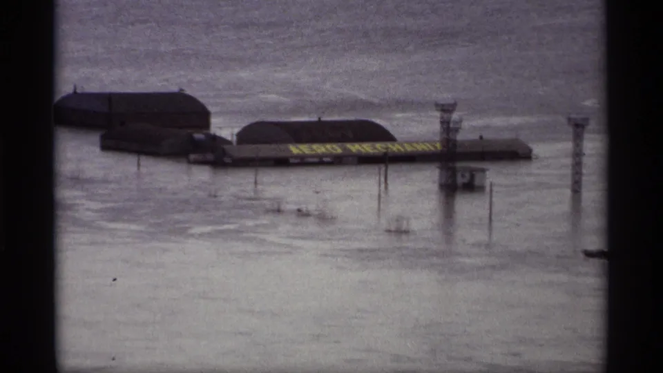 1969 Saint Paul floodwater surrounds riverside buildings, utility structures, and a partially visible AERO MECHANICS sign.