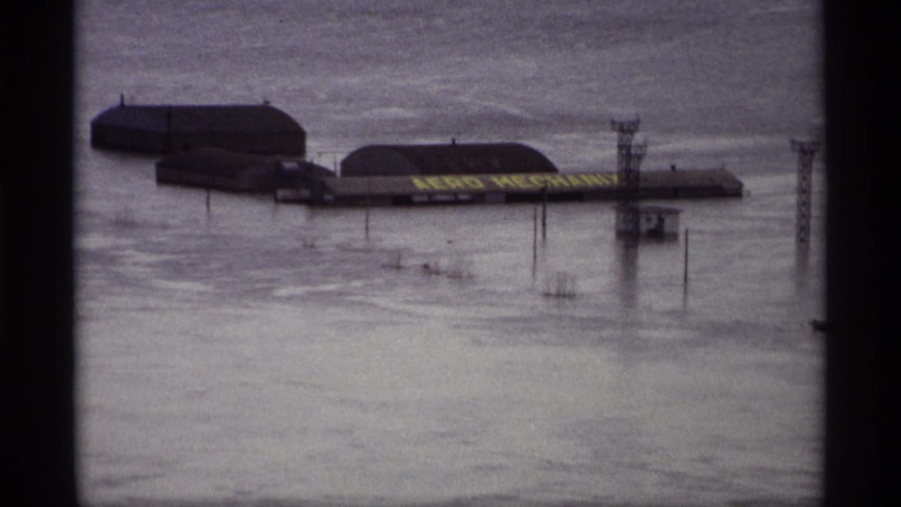 Flooded riverside buildings and utility posts seen through dark 8mm frame borders.