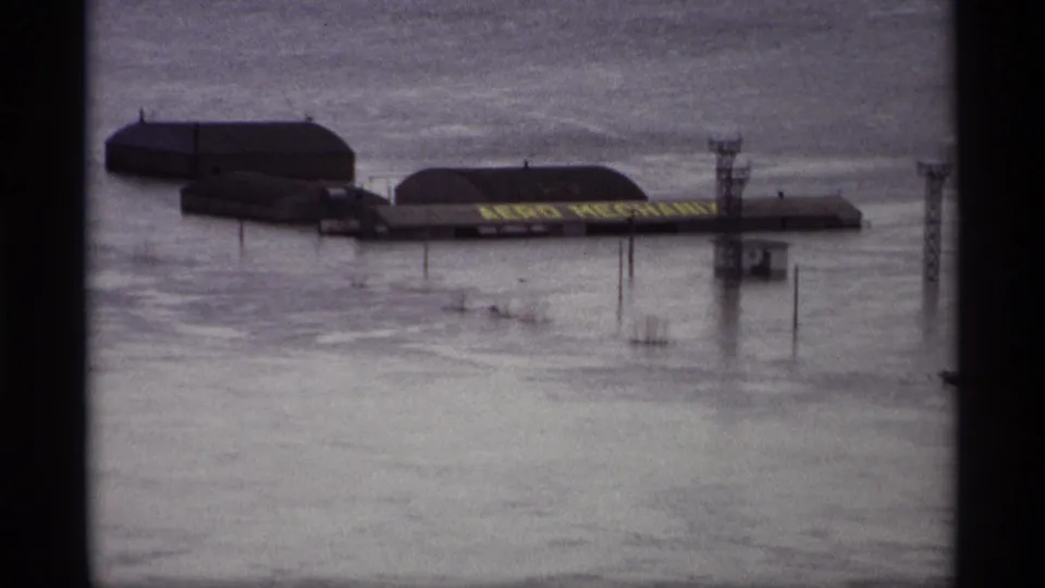 Saint Paul flood scene shows low buildings, a partially visible sign, and utility posts standing in high water.