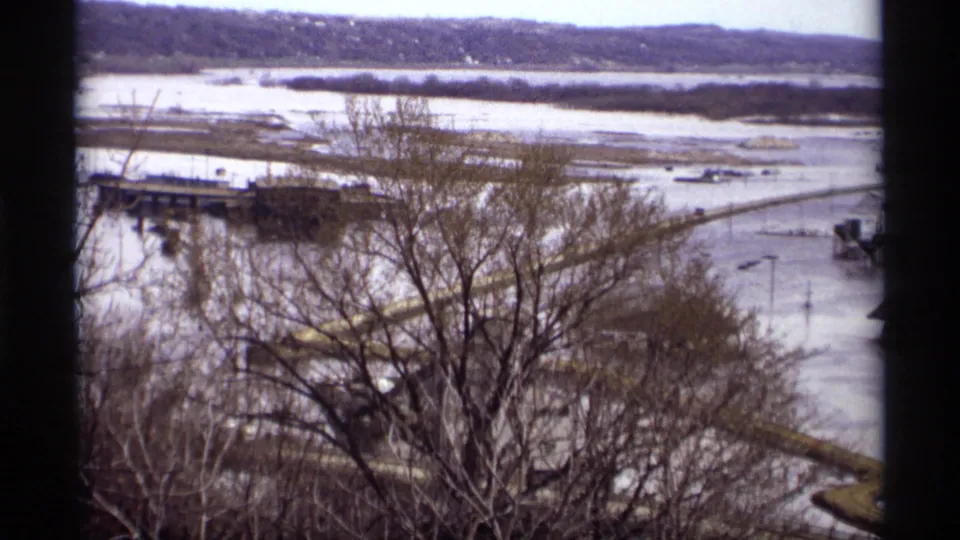 Elevated 1969 Saint Paul view of floodwater around a waterfront bridge or pier, with bare trees, shoreline, and roadways visible.