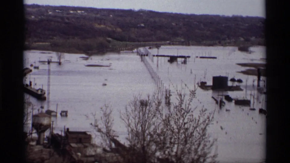 1969 Saint Paul flood view with submerged dock lines, distant houses, bare trees, and soft 8mm frame edges.