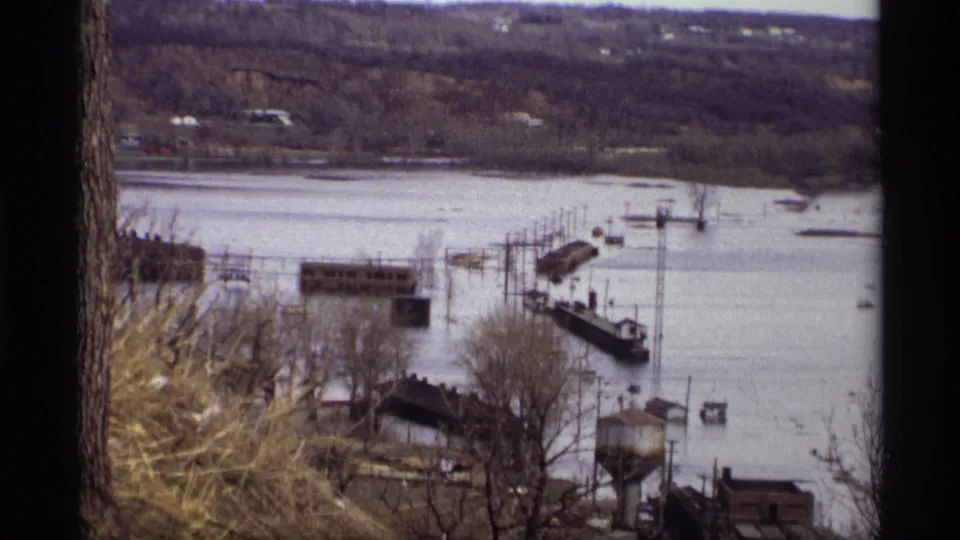 Saint Paul, Minnesota flood footage from 1969, viewed from a hillside across waterlogged docks and riverside buildings.