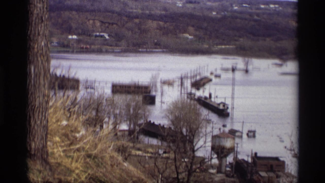 Flooded river with submerged docks and boats seen from a wooded overlook.