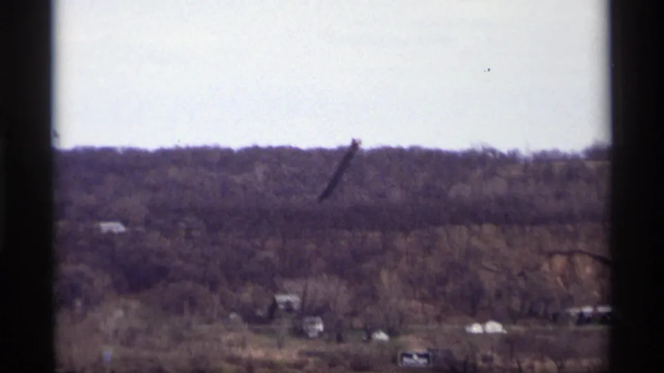 Soft 1969 home-movie frame from Saint Paul, showing a wooded hillside, small distant structures, and floodplain trees near the river.