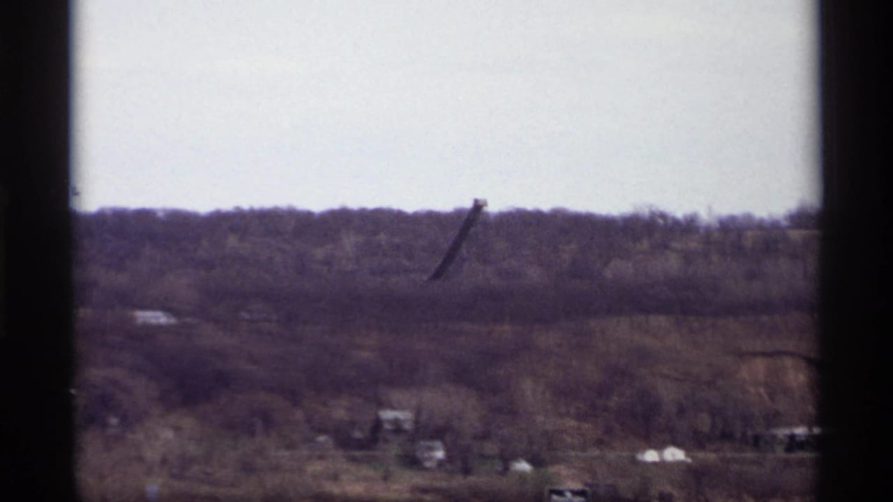1969 Saint Paul home-movie view of a wooded ridge and dark raised industrial apparatus framed by a window.
