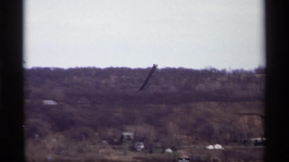 1969 Saint Paul home-movie view of a wooded ridge and dark raised industrial apparatus framed by a window.