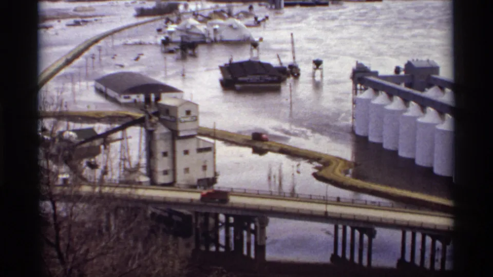1969 Saint Paul flood scene showing an industrial riverfront, white silos, a bridge, and water covering low ground.