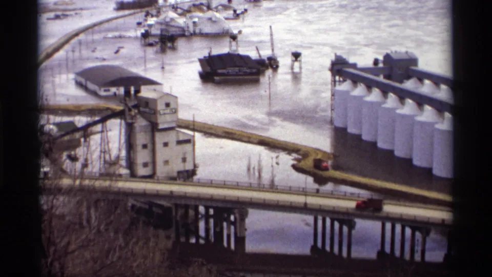1969 Saint Paul 8mm frame showing a red car on a bridge near floodwater, industrial buildings, and white riverside silos.