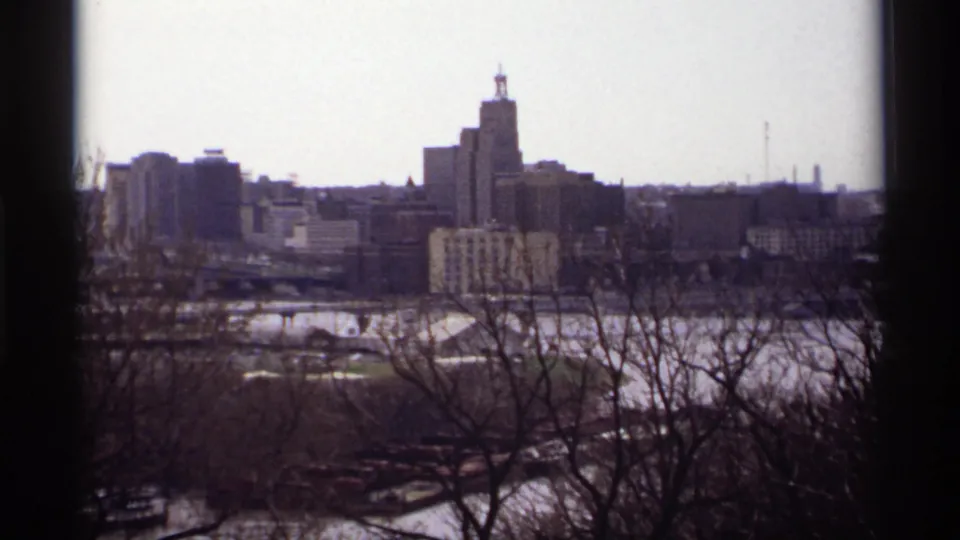 1969 8mm view of Saint Paul skyline with bare trees in the foreground and a tall building rising near the center.