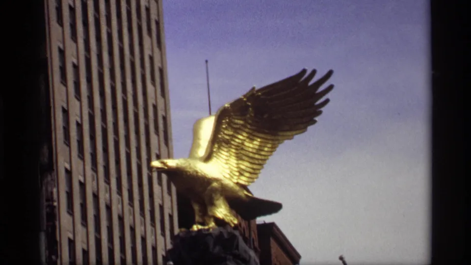 Final 1969 Saint Paul view of the gold eagle statue on a dark base, set against a tall facade and clear blue sky.