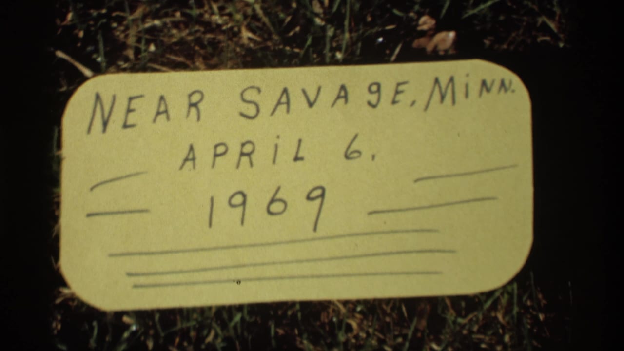 Close 8mm frame of a yellow handwritten label on grass identifying near Savage, Minnesota, April 6, 1969.