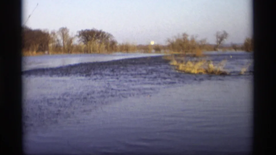 The camera looks across floodwater toward bare trees and brush, with no people visible in this frame from the 1969 Savage, Minnesota clip.