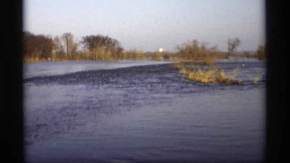 A wider home-movie view shows open floodwater, a brushy island or shoreline, and bare trees in Savage, Minnesota in 1969.
