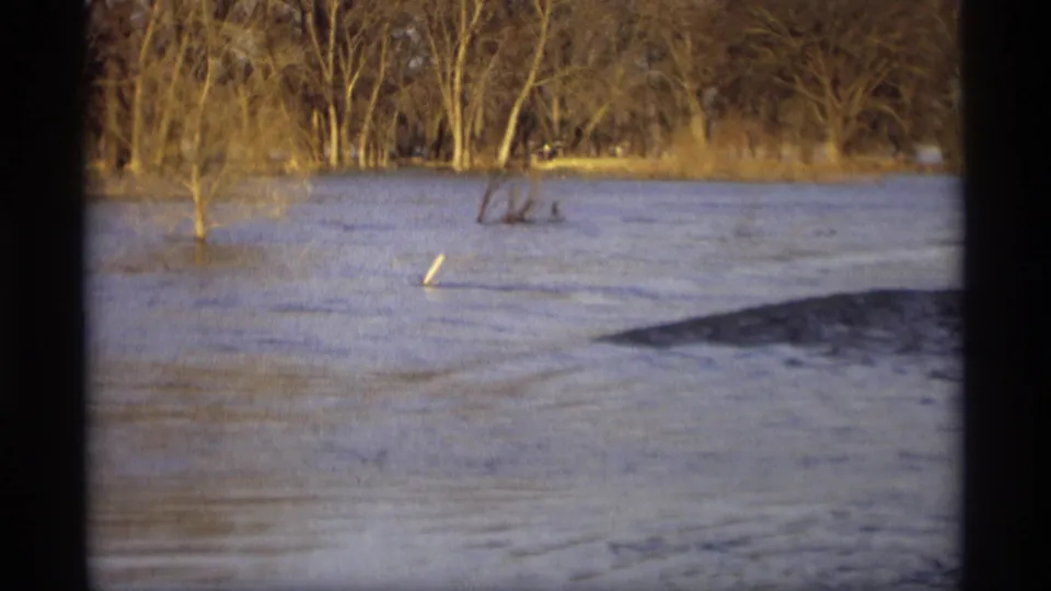 1969 Savage, Minnesota 8mm frame of a flooded countryside waterway with leafless trees and brush standing in high water.