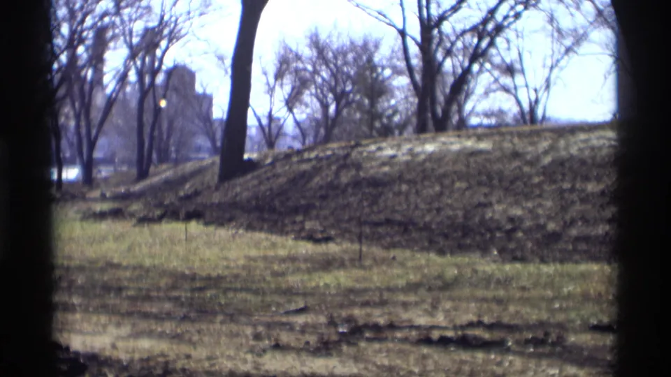 A soft 8mm frame of a Savage, Minnesota park landscape with leafless trees, sloped grass, and a pale bright background.