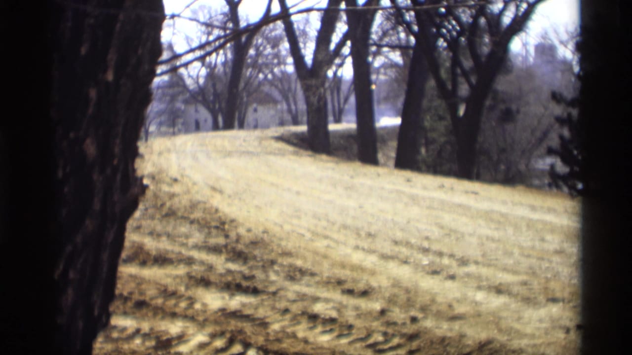 1969 8mm view in Savage, Minnesota of a graded embankment and bare trees with small distant buildings in the background.