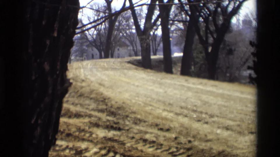 Savage, Minnesota home-movie frame showing a winter-bare tree line and graded slope in soft 8mm color.