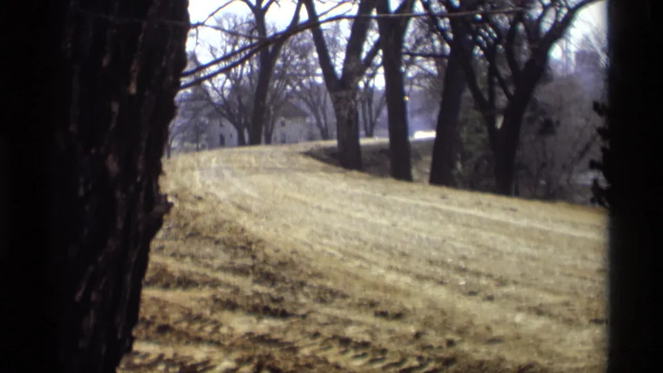 1969 Savage, Minnesota landscape frame with a graded embankment, leafless trees, and distant structures beyond the slope.